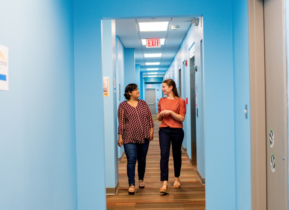 two smiling people walking down a blue hallway while talking