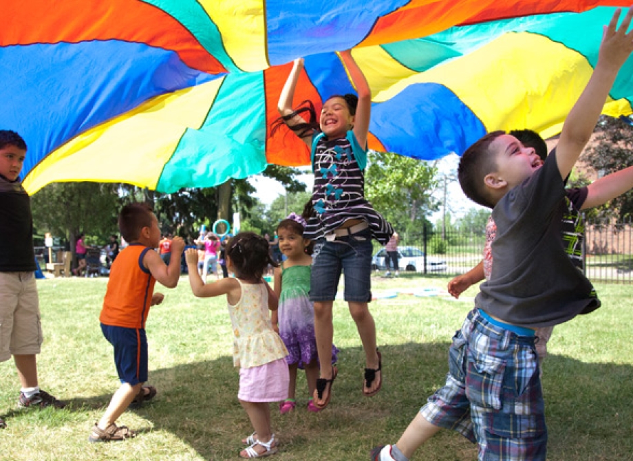 kids playing outdoors with a multicolored parachute 