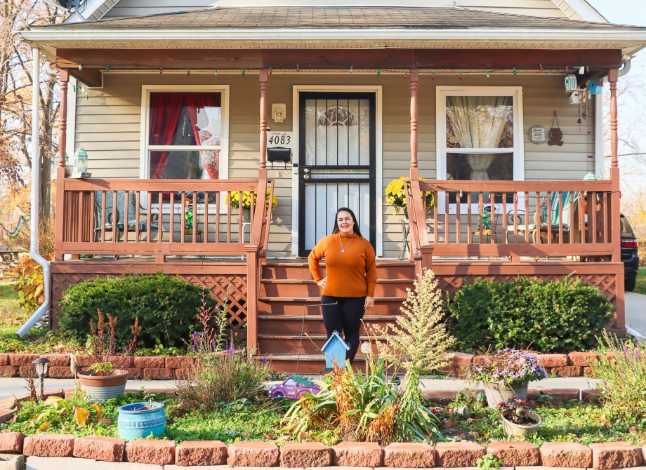 a woman stands outside her home surrounded by her garden