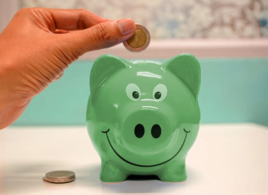 a hand putting a coin into a green piggy bank